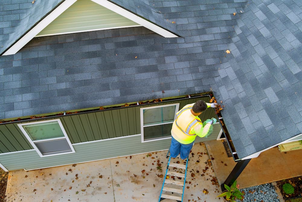 Professional cleaning gutters from a rooftop before winter weather