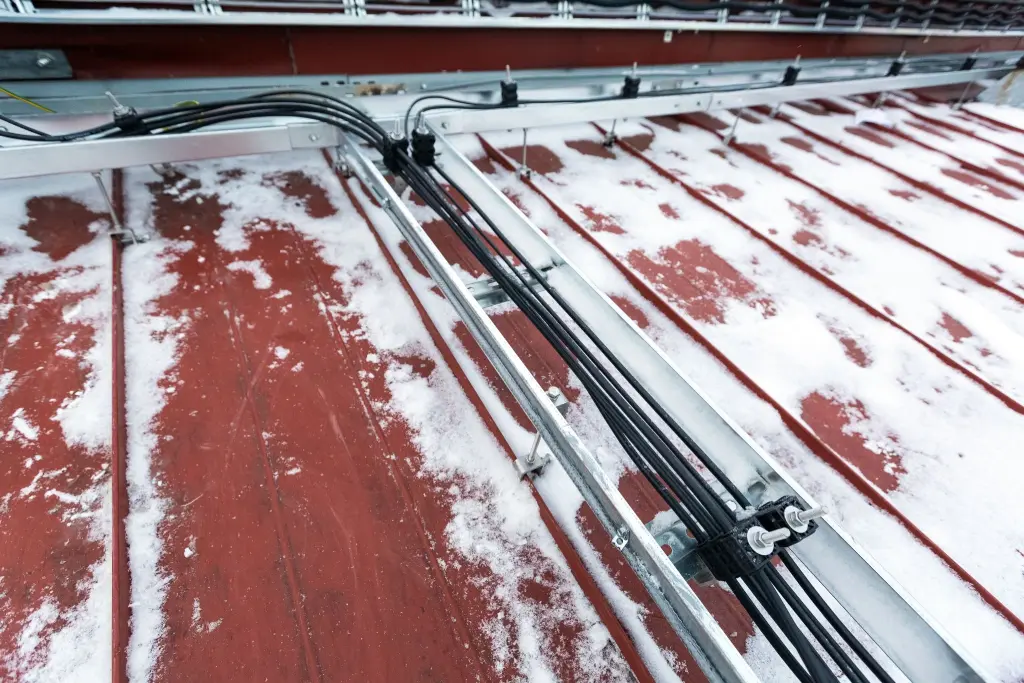 Black cables secured to metal support rails above a snow-dusted roof