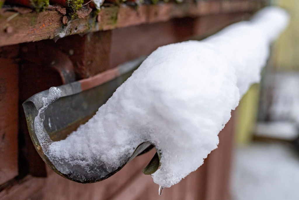 Close-up of snow and ice buildup inside a half-round metal gutter