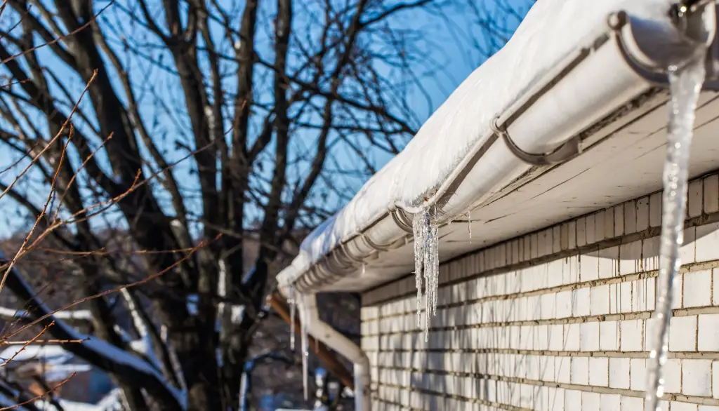 Long icicles hanging from a gutter beneath a snow-covered roof