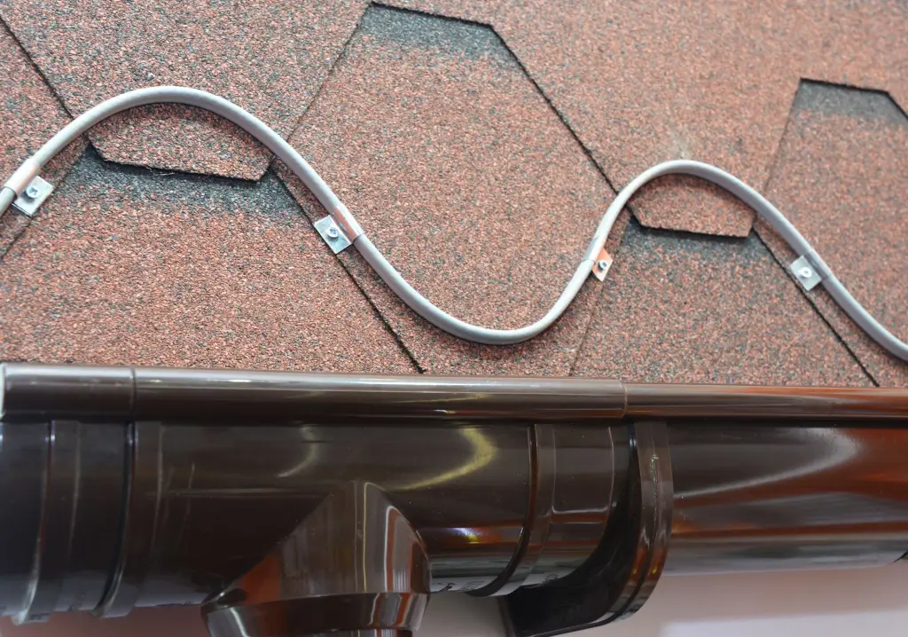 Roof heating cable clipped in loops above a gutter on asphalt shingles